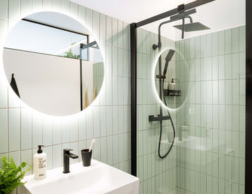 Badezimmer mit Dusche, Waschbecken und beleuchtetem Spiegel