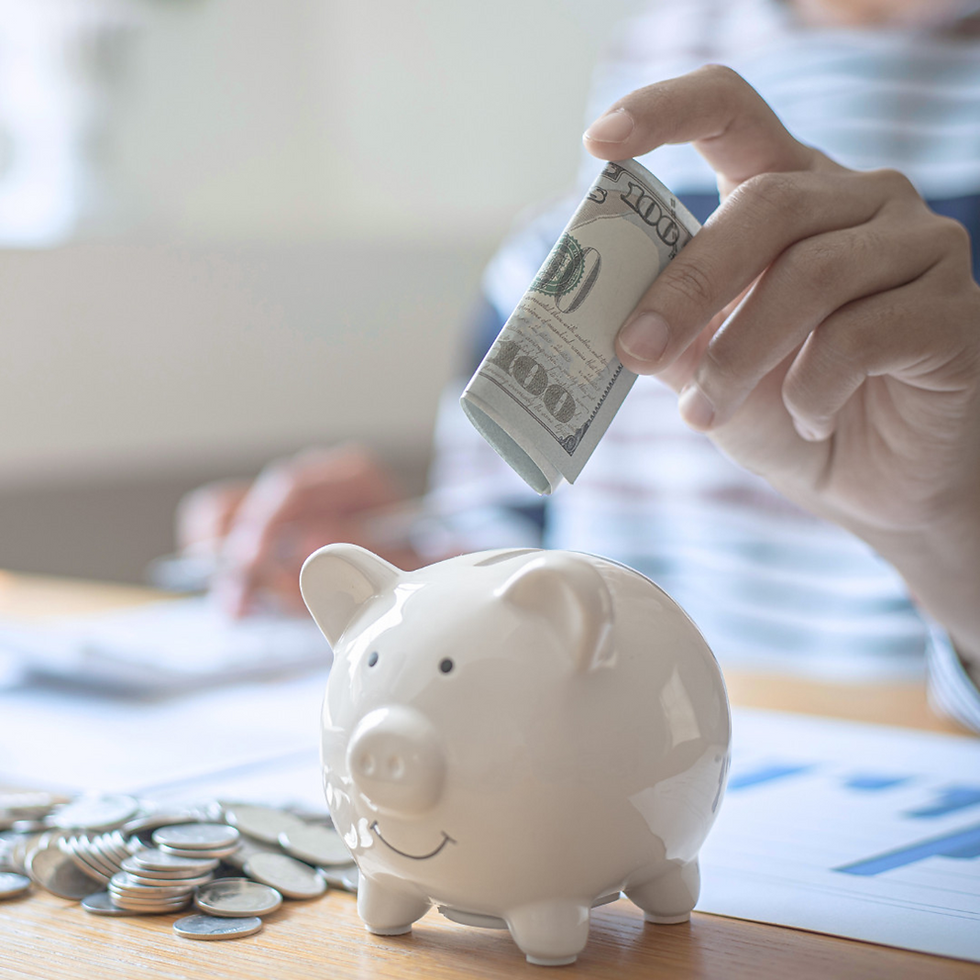 Person saving money by putting a 100 dollar bill into a piggy bank, symbolizing financial savings and building an emergency fund.