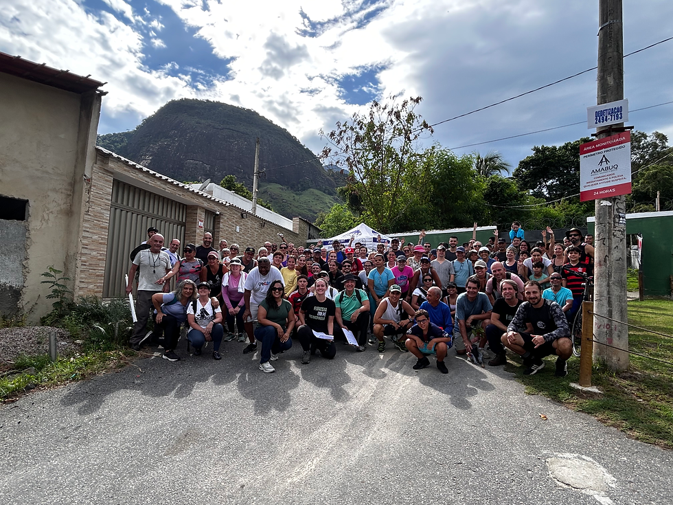 Grupo grande posa sorrindo numa rua, com montanha ao fundo e céu nublado;