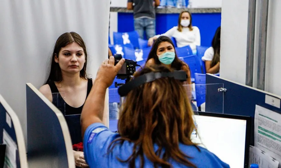 Na imagem podemos ver uma jovem sendo fotografada por uma funcionária do Detran.