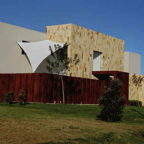 Casa de piedra iluminada por el sol con la ventana cubierta con una vela mediterranea dando sombra al cuarto que tiene una venta donde da el sol. En Buenos Aires, argentina. 
