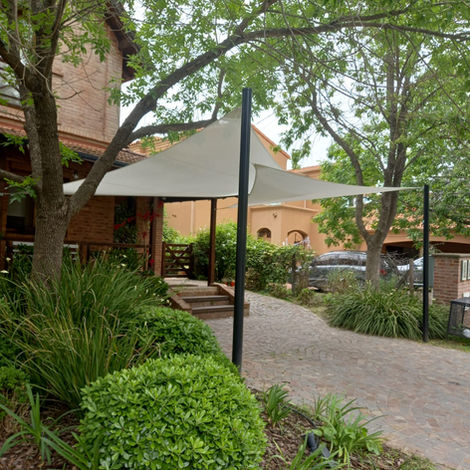 Vela de sombra para la cochera de una casa grande. La casa tiene árboles alrededor. 