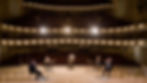 Wind quintet performing on a lit stage in a concert hall