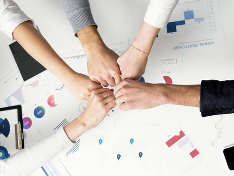 Five hands in a fist bump over a desk with charts and graphs