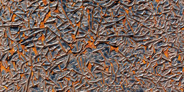 Close-up of cracked rusted metal surface with orange and dark gray textures forming abstract patterns