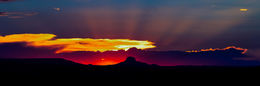Sunlight breaking through clouds above Cabezon Peak with dramatic color contrast