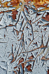 Close-up of peeling white paint over rusted metal with sharp cracked edges and layered texture