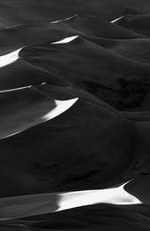 Sand dunes with bright edges and deep shadows at sunset in black and white
