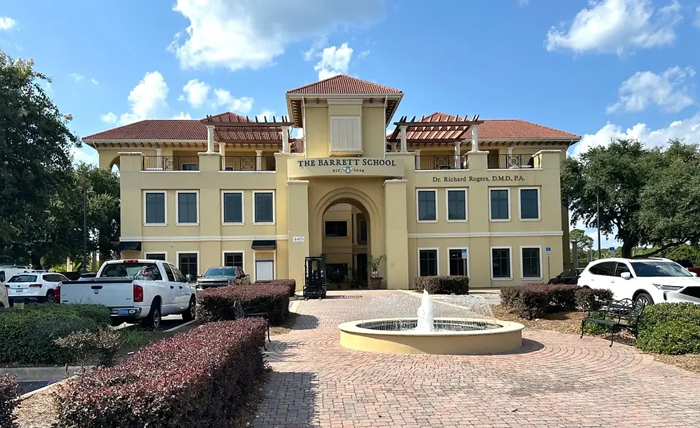 Front exterior of The Barrett School building in Destin, Florida, with a fountain and landscaped walkway.