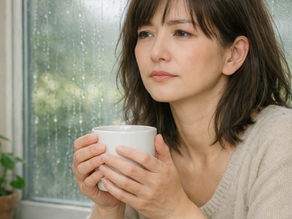 梅雨の雨を眺めながら温かい飲み物を持つ女性。不調や疲れを感じる梅雨時期のイメージ