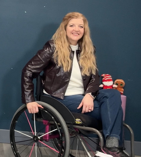 Image of Tennille, wearing a white shirt and mauve jacket, sitting in her wheelchair