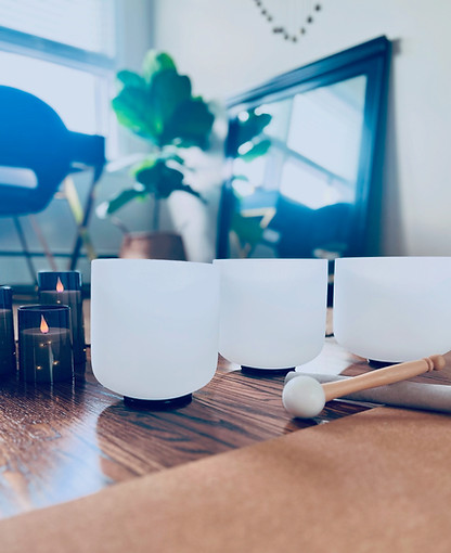 Three singing bowls and three candles sitting in front of a mirror, plant, and desk