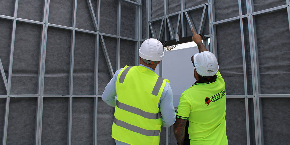 Construction workers installing a wall frame, wearing reflective vests and hard hats.