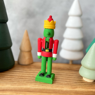 The Grinch Nutcracker doll, painted in a red santa coat with belt in black and gold belt buckle. The rest of the wooden nutcracker is painted in green and black shoes. The hat is yellow and red.