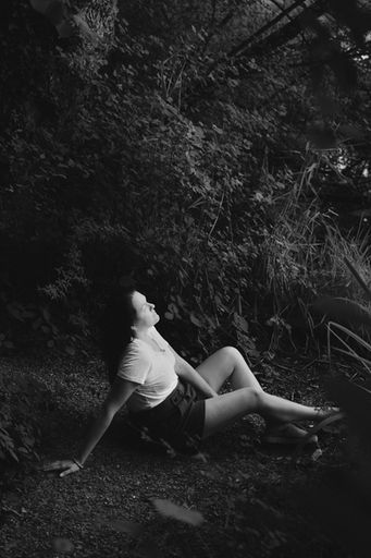 Schwarz-Weiss-Bild einer jungen Frau, die im Gras liegt und nach oben schaut, Brand-Fotografie mit Stimmung