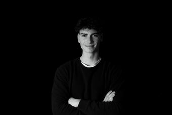 Junger Mann in Schwarz mit verschränkten Armen vor schwarzem Hintergrund, Corporate-Portrait im Studio
