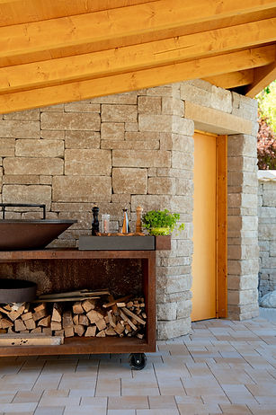 Outdoor-Küche aus Naturstein mit Brennholz und Holzdach, Fotografie für Brands und Unternehmen