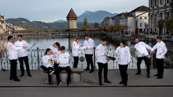 Kochteam in weissen Jacken vor Wasserturm und Bergen in Luzern, Teamfotografie für Gastronomie