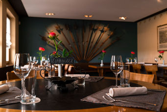 Gedeckter Tisch im Restaurant mit roten Blumen und Gläsern vor dunkelgrüner Wand, Gastronomiefotografie Luzern
