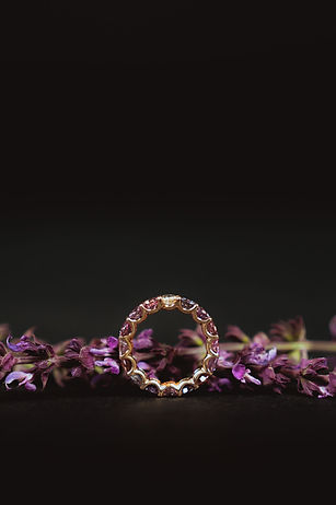 Goldener Ring mit rosa Steinen vor dunklem Hintergrund und violetten Blüten, Schmuckfotografie in Luzern
