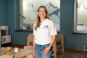 Frau in weissem Poloshirt lächelt vor blauer Wand im Geschäft, Mitarbeiterportrait für Unternehmen