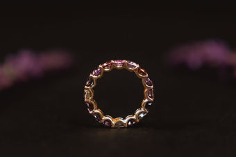Goldener Ring mit rosa Steinen vor dunklem Hintergrund und violetten Blüten, Schmuckfotografie in Luzern
