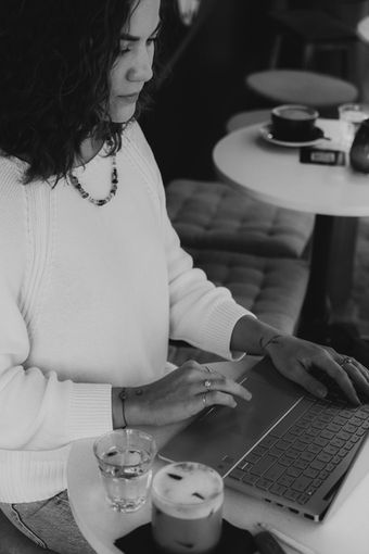 Schwarz-Weiss-Aufnahme einer Frau am Café-Tisch mit Kaffee und Laptop, persönliches Portrait im Alltag