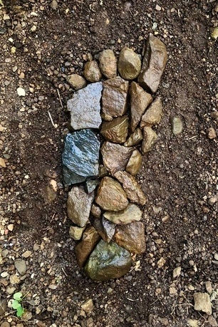 Sculpture of a foot made of pebbles on a bare patch of earth