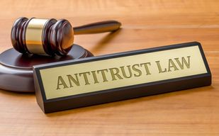 Gavel on wooden desk beside a gold nameplate reading "ANTITRUST LAW." The setting implies a legal or courtroom atmosphere.