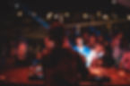 A DJ with headphones plays music at a crowded, dimly lit event with colorful lights and dancing people.