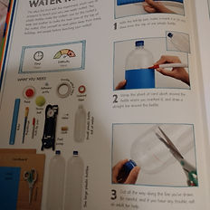 The Materials used for making a water jet spaceship of Two pop bottles (one smaller than the other), tennis ball, cardboard, cork, foot pump with tube, ruler, marker, knife, inside and outside tape, red Paint and a paint brush. The picture also shows cutting bottles at 10" each.