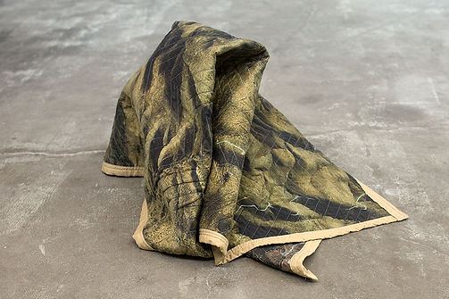 A blanket with satellite images of the border, in a strange pile on the floor.