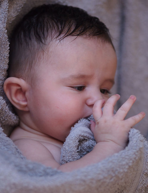 Gros plan d’un bébé emmitouflé dans une couverture, main près du visage, ambiance douce et intime.