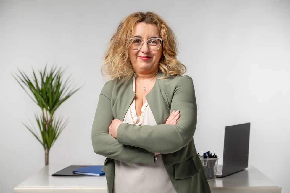 Donna sorridente in giacca verde con braccia incrociate in ufficio.