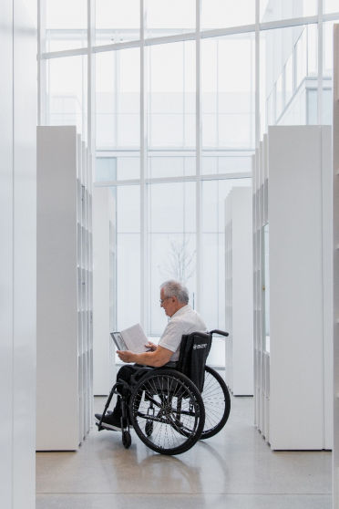 Thumbnail: Elderly man in wheelchair reads in library; Essential LC104; white background.
