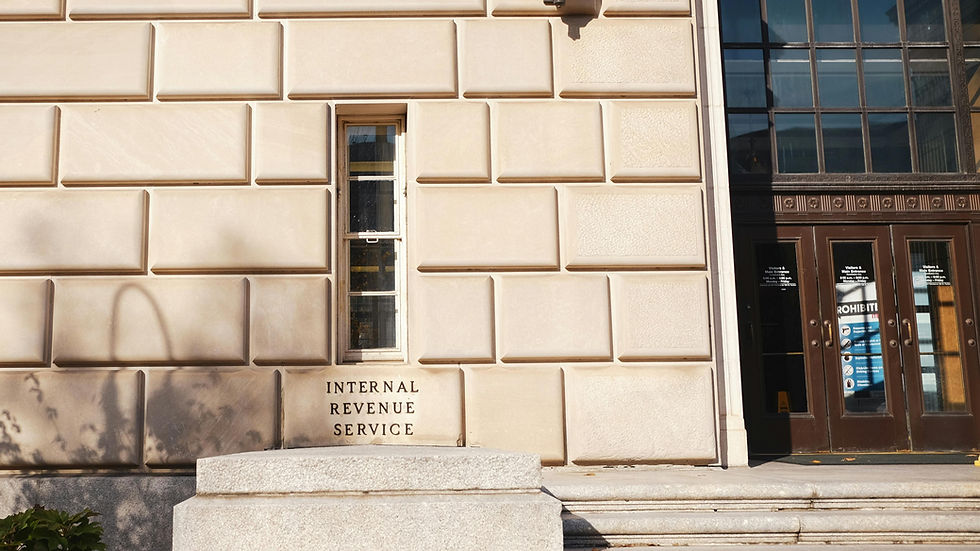 Beige building facade with a window, and dark doors. "Internal Revenue Service" is engraved. Shadows cast on the textured wall.
