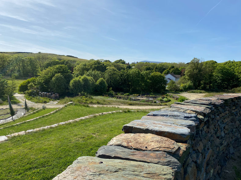 a circular stone walls around green fields and surrounded by orchards.