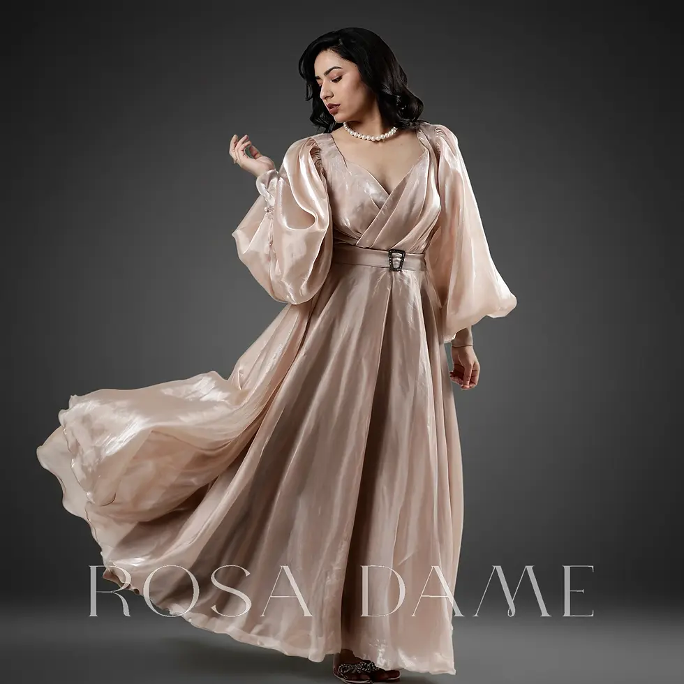 Front view of champagne organza satin gown with deep wrap neckline, statement belt, and flowing A-line silhouette on dark gra