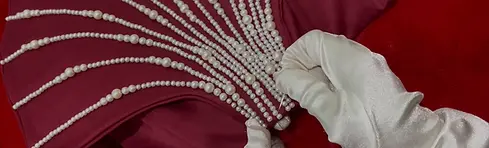 Close-up of handcrafted pearl detailing being stitched onto burgundy fabric with precision gloves