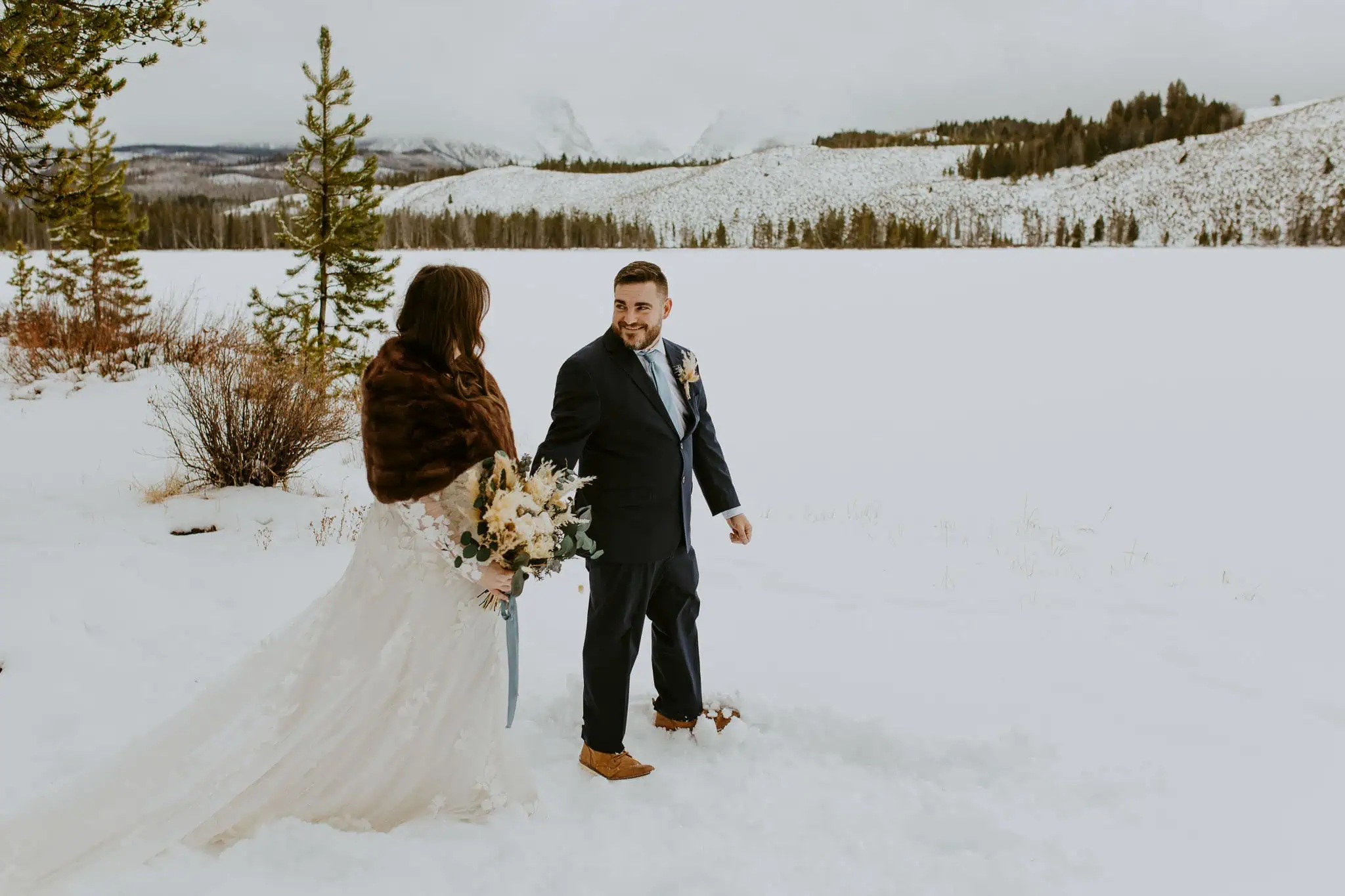 groom leading bride across the snow in front of mountains