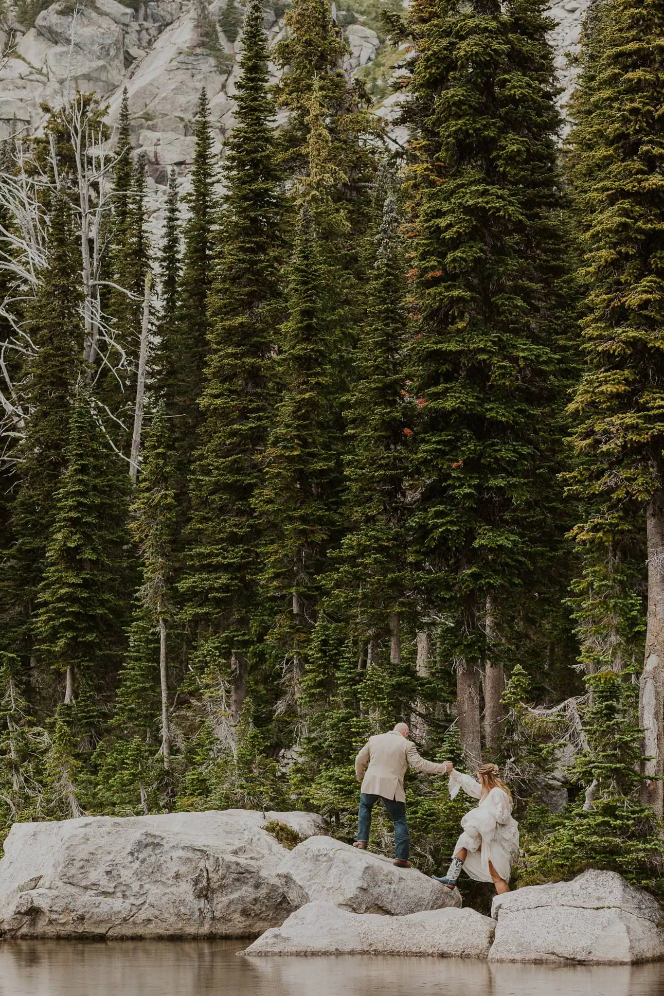 a bride and groom climbing onto a rock