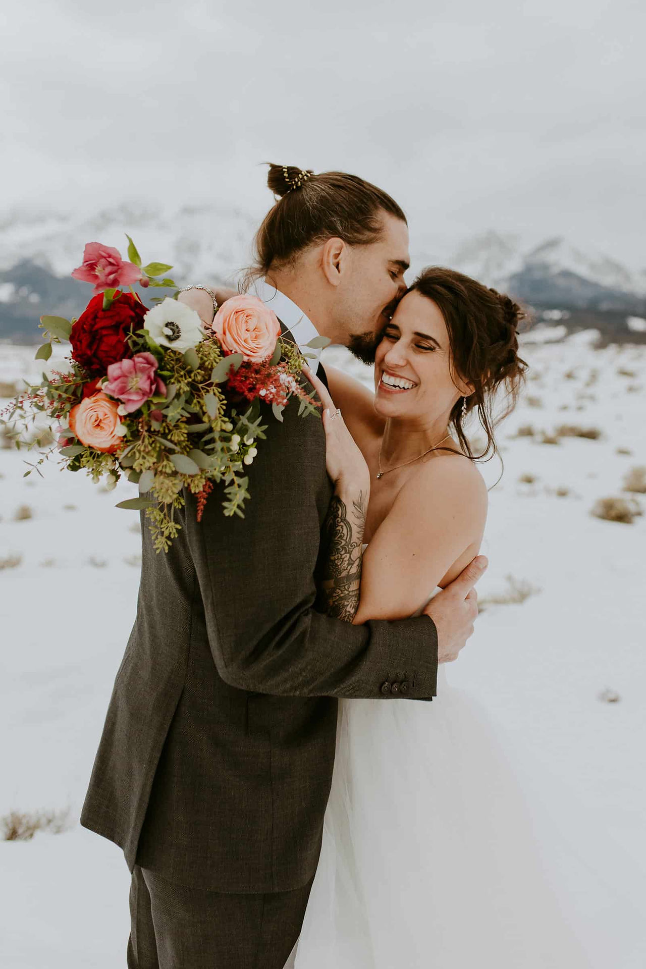 a groom kissing a bride's forhead in the snow