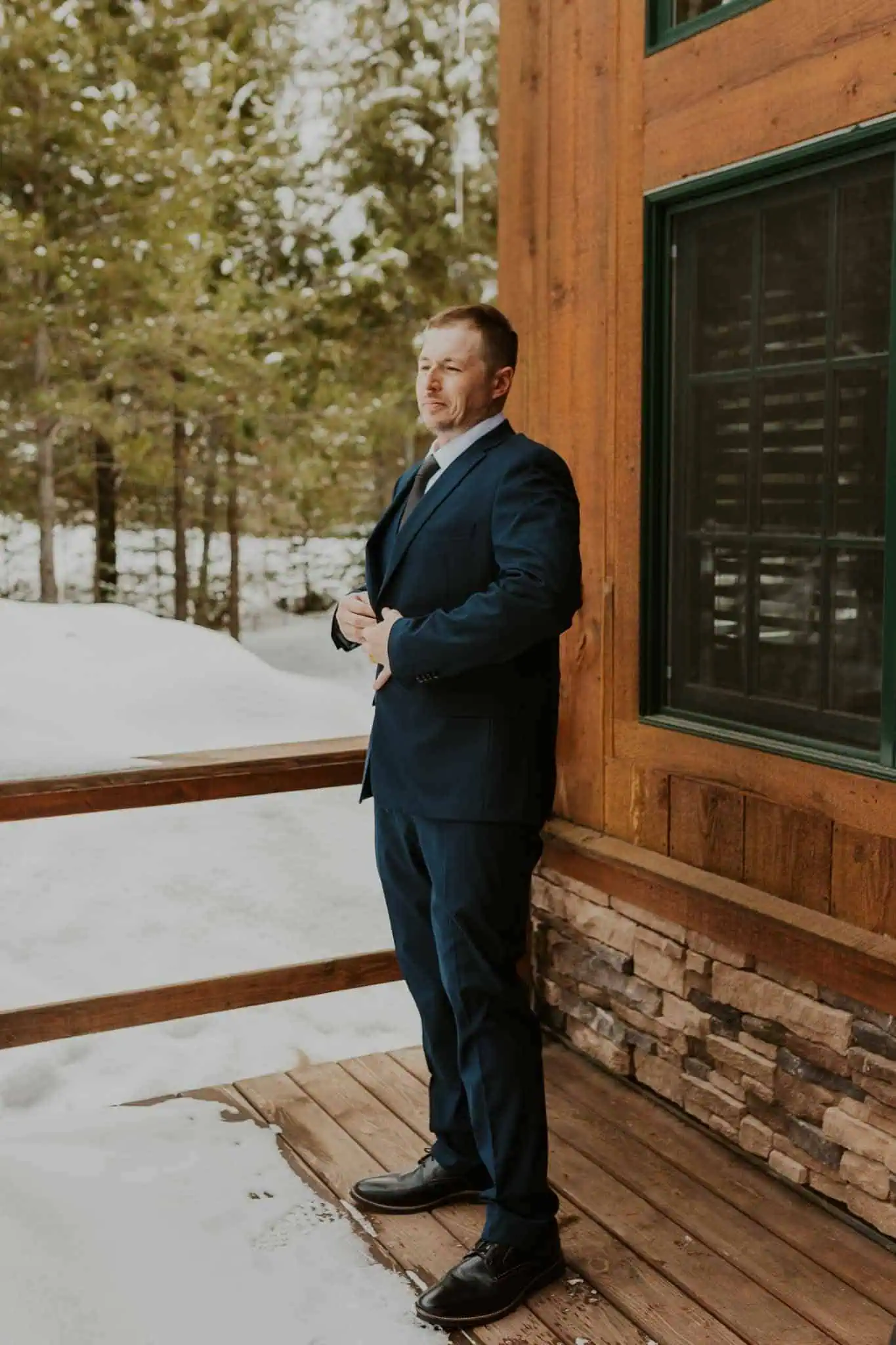 groom buttoning his jacket on the porch of a cabin
