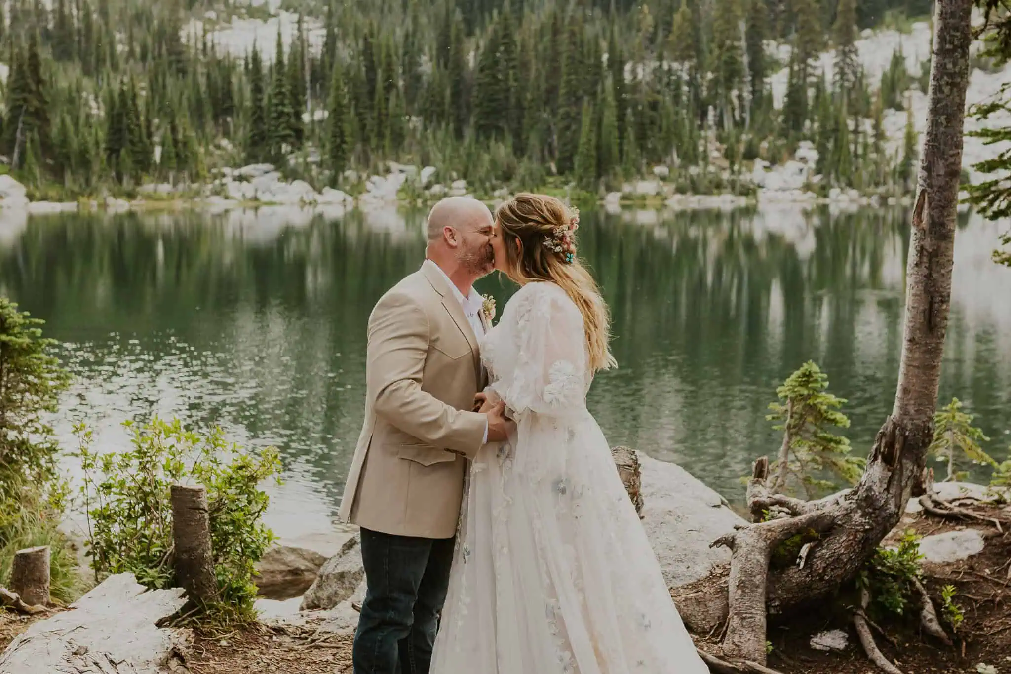 bride and groom kissing in front of a lake in the mountains