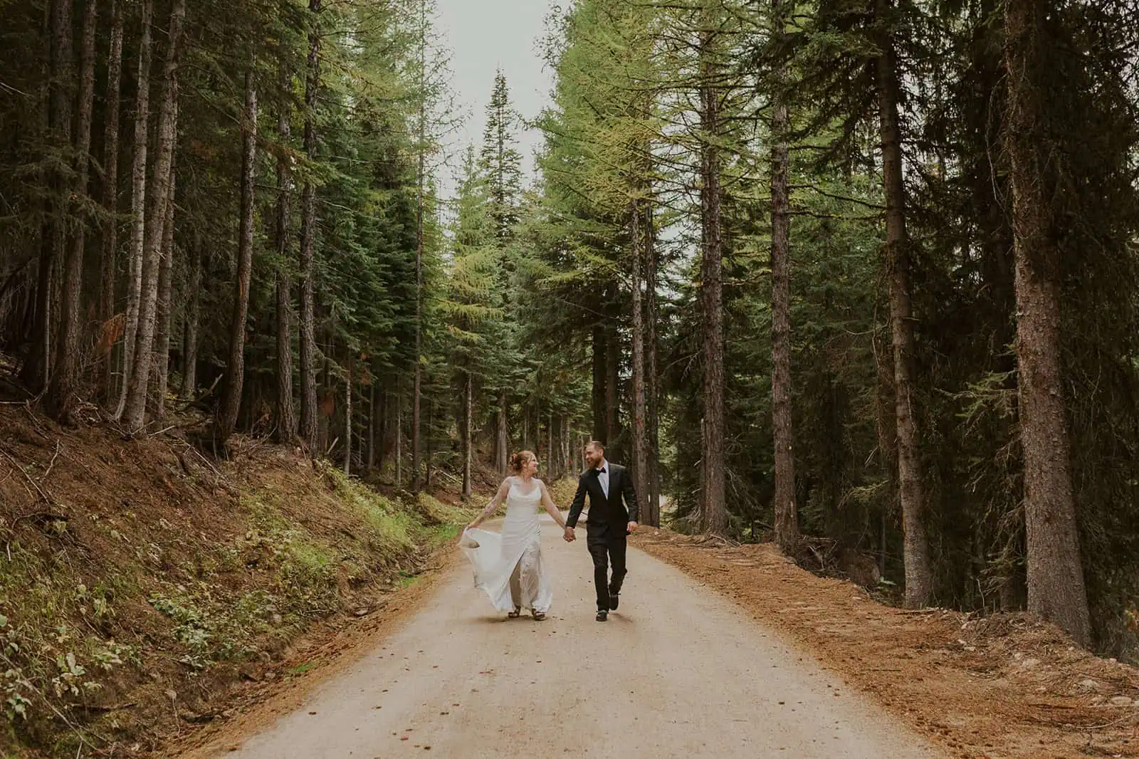 bride and groom holding hands running through a forest