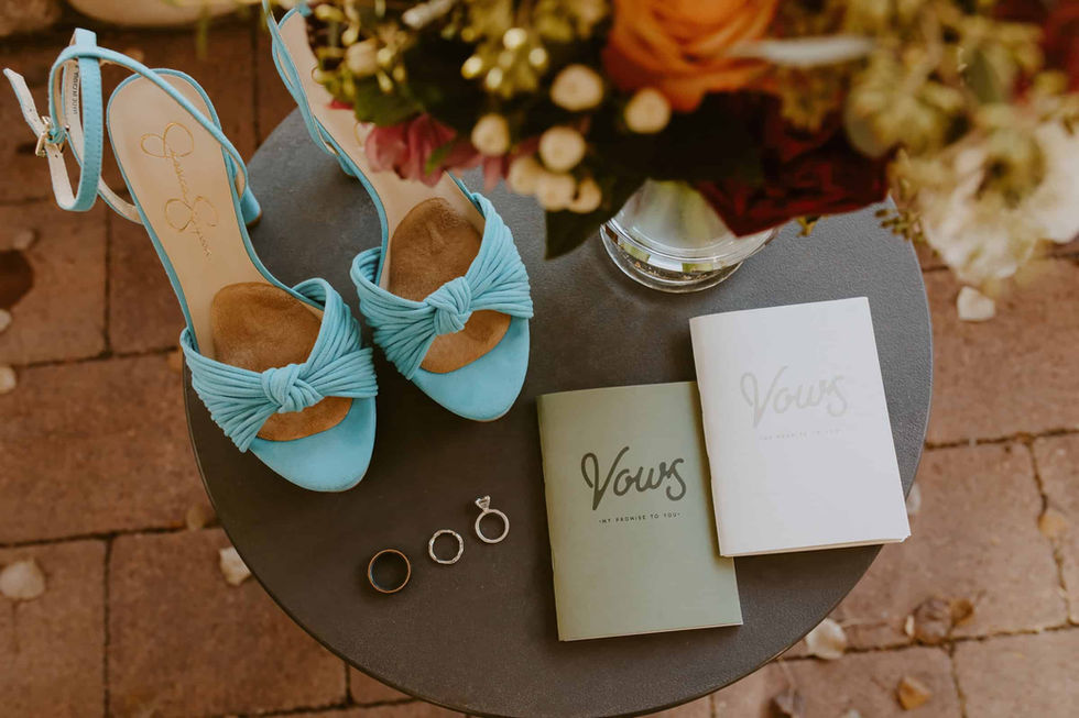 blue wedding heels on a table with flowers, vow books, and rings