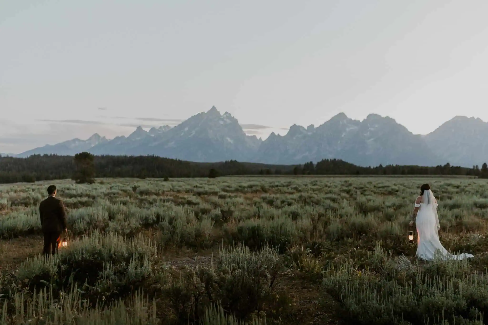 a bride and groom holding lanterns in front of the tetons