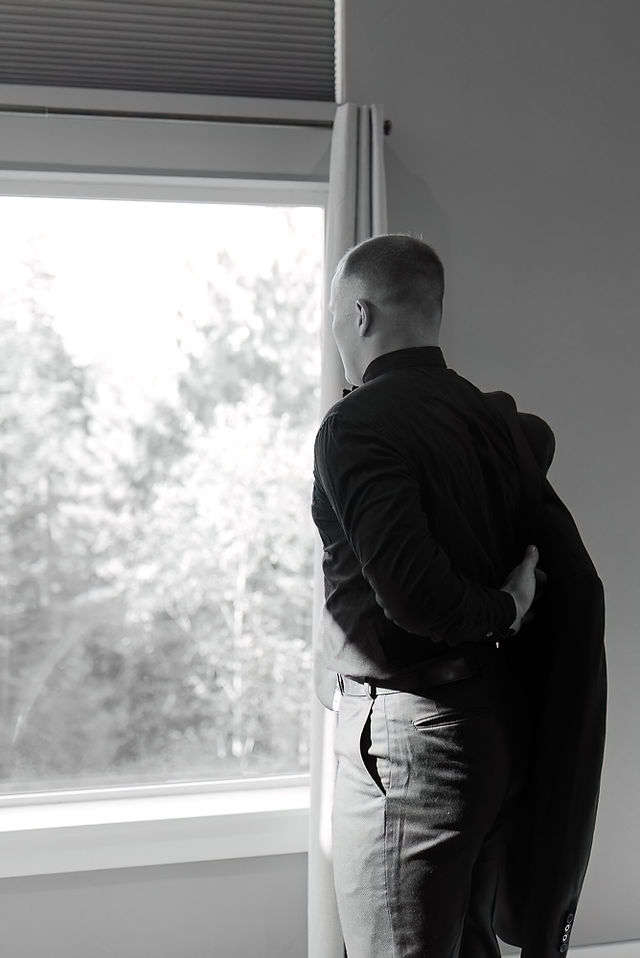 groom getting ready by putting on his suit jacket by a window