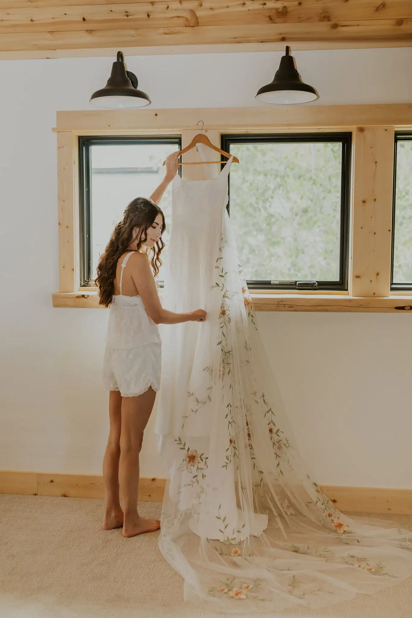 bride holding her wedding dress by a window
