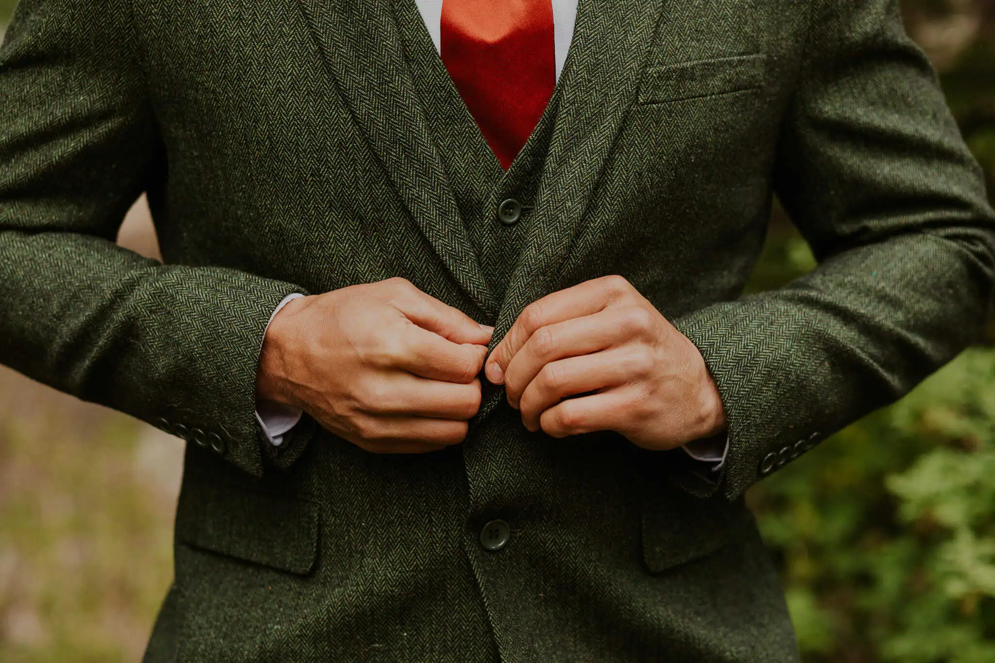 a groom buttoning up his green suit